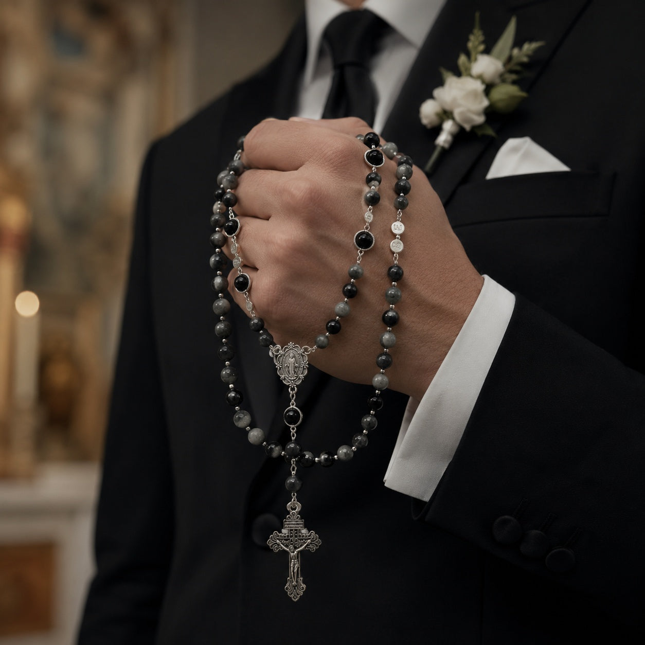 Men’s Catholic wedding rosary for groom with black and gray beads, silver crucifix, and Virgin Mary medal held with a formal suit