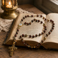 Men’s Catholic rosary with brown natural stone-style beads, vintage gold crucifix, and religious medal displayed on an old stone church setting.