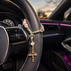 Personalized Catholic car rosary displayed on a car steering wheel, featuring pink beads, gold details, and a crucifix