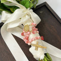 Pink Catholic wedding rosary for bride with gold crucifix, Marian medal, and rose accent beads styled on a bridal bouquet