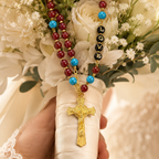 Red Catholic wedding rosary displayed on soft bridal lace with gold crucifix, LOVE beads, and elegant wedding accessories