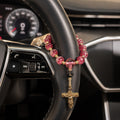 Red Catholic car rosary wrapped around a steering wheel with textured red beads, personalized initial charm, and gold crucifix