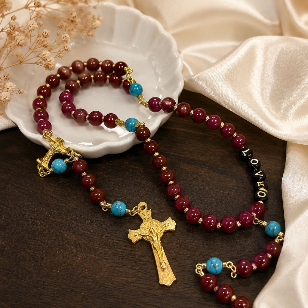 Red Catholic rosary with gold crucifix, turquoise accent beads, and LOVE letter beads displayed on a white ceramic dish