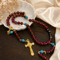 Red Catholic rosary with gold crucifix, turquoise accent beads, and LOVE letter beads displayed on a white ceramic dish