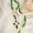 Catholic wedding rosary for bride hanging on a church pew with white ribbon and flowers, featuring emerald green beads and gold cross pendant