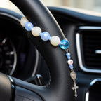 Personalized blue steering wheel rosary with white beads, silver crucifix, and Catholic medal, designed as a meaningful driver gift