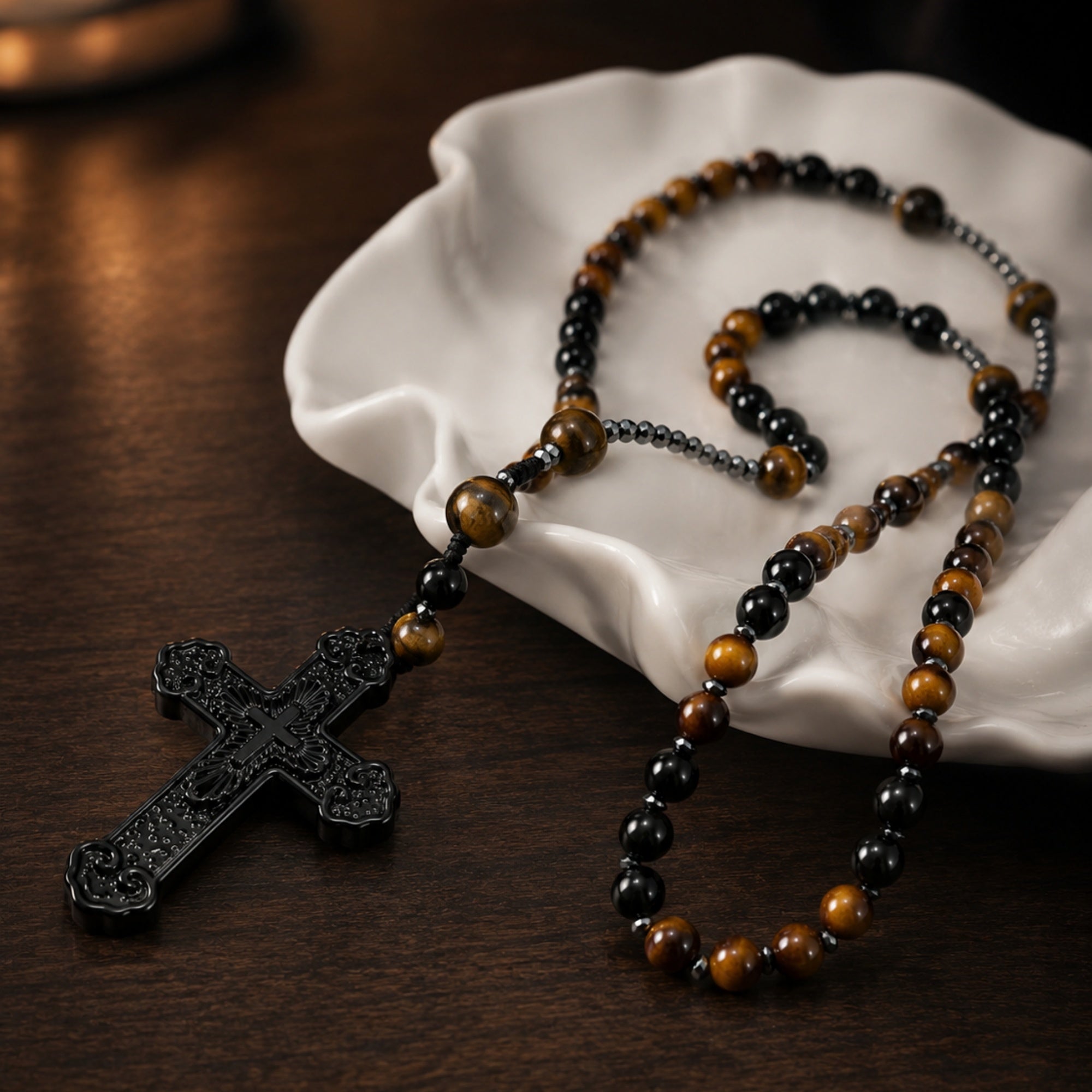 Tiger eye Catholic rosary beads for men with a black crucifix displayed on a white ceramic dish and dark wooden table