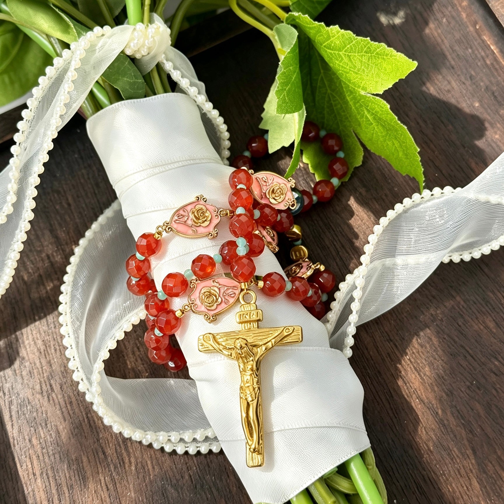 Burgundy Catholic wedding rosary for bride with gold crucifix, turquoise accents, and rose medals styled on a bridal bouquet
