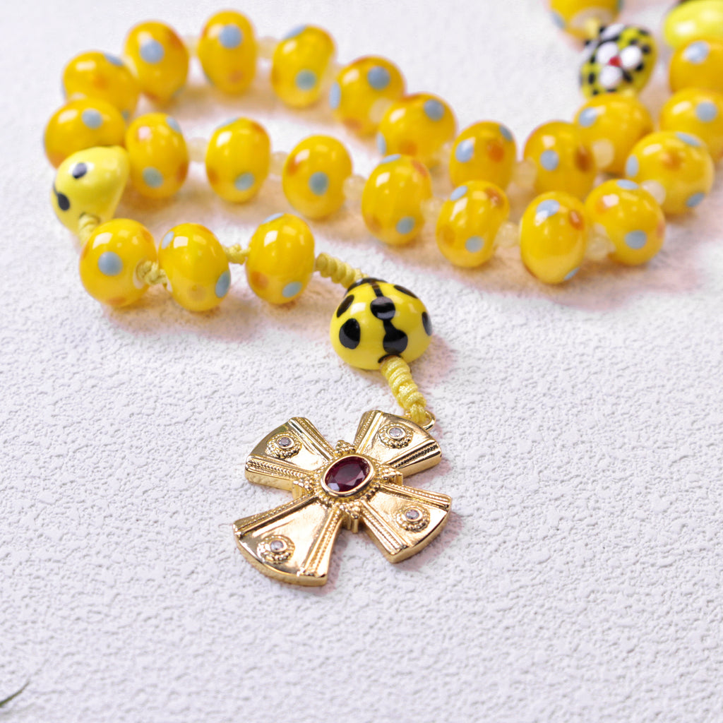 Close-up of a yellow Catholic rosary featuring a gold-tone crucifix, ladybug bead accents, and colorful prayer beads with a cute faith-inspired design.
